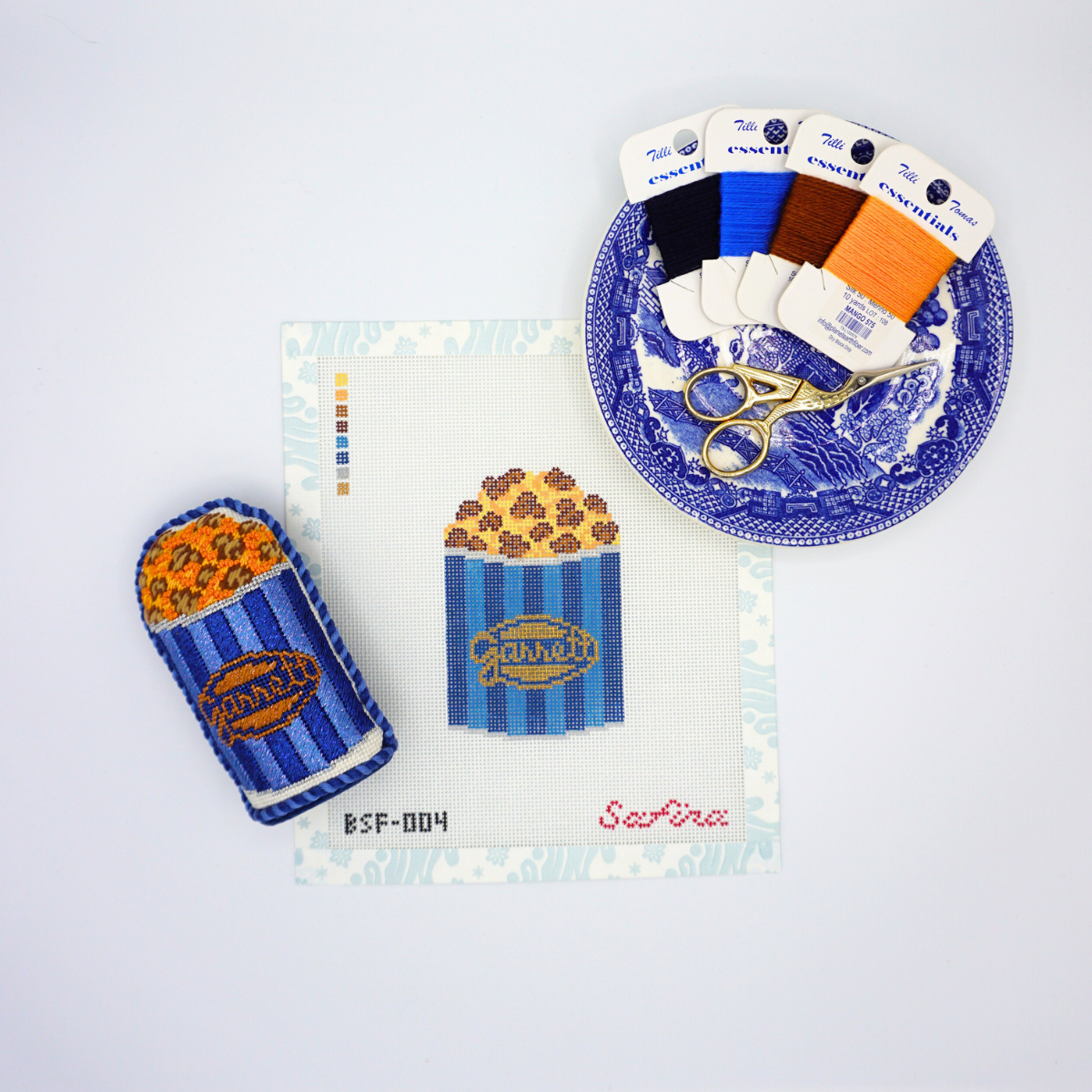 Caramel and cheese mix Chicago popcorn in blue striped tin needlepoint canvas design with finished popcorn standup, essentials thread, and scissors